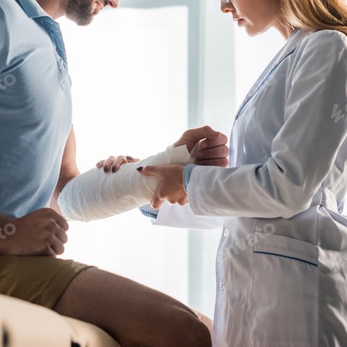Preview: cropped view of orthopedist touching injured hand of bearded man
