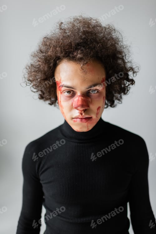 Preview: injured african american man with broken nose and bleeding face looking at camera isolated on grey