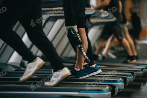 Preview: cropped shot of sportsman with artificial leg running on treadmill at gym with other people