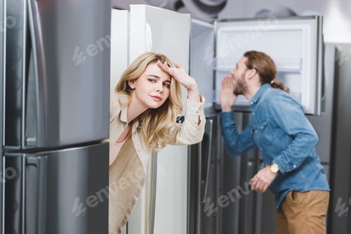 Preview: selective focus of curious girlfriend and boyfriend looking at fridge on background in home