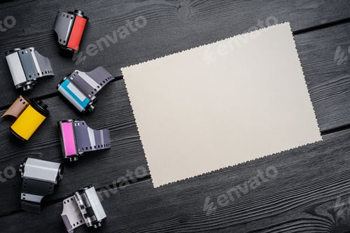 Preview: Colorful film canisters and blank photo card with scalloped edges on a dark wooden table.