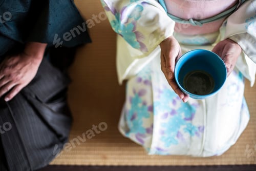 Preview: Japanese man and woman kneeling on floor during tea ceremony, holding blue tea bowl.