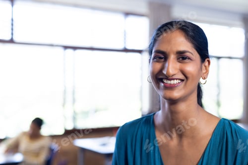 Preview: Smiling indian female teacher in classroom, standing and looking at camera in school, copy space
