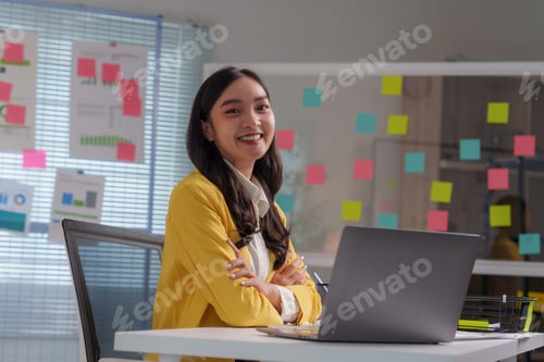 Preview: Asian businesswoman smiling with arms crossed sitting at desk in modern office