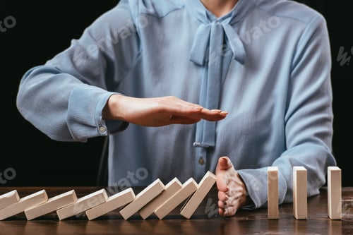 Preview: cropped view of woman sitting at desk and preventing wooden blocks from falling