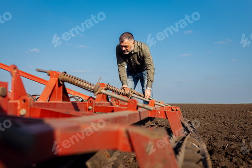 Preview: Portrait of mature farmer standing in field preparing to cultivate the land with a tractor.