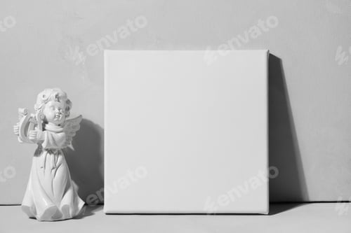 Preview: White canvas board and angel figurine against grey wall.