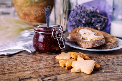 Preview: Homemade sugar honey cookies, raspberry jam in jar, bread and butter, knife, on a wooden background