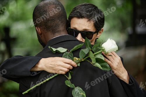 Preview: Senior Woman with Flower Hugging Husband Grieving Loss at Cemetery
