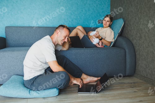 Preview: Parents with baby sitting on sofa at home with laptop and talking online. A young family