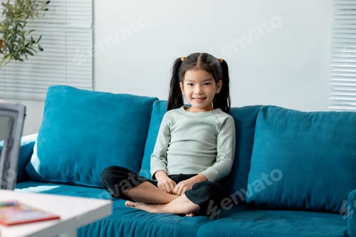 Preview: Smiling asian girl sitting on blue sofa in living room