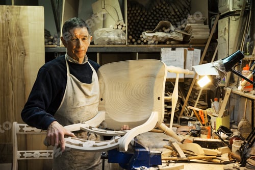 Preview: Man standing at a work bench in a carpentry workshop, working on a wooden chair.