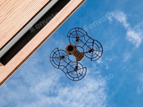 Preview: Worm's eye view of a drone with propeller guard flying against a blue sky