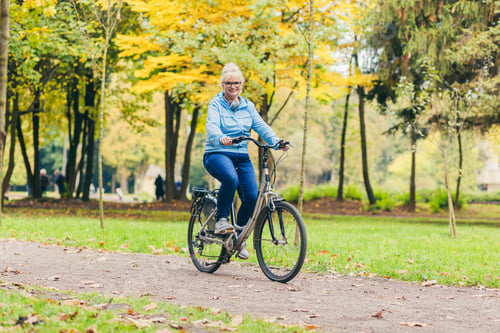 Preview: Senior beautiful blonde woman rides a bike in the park, in the woods, in nature, listens to music