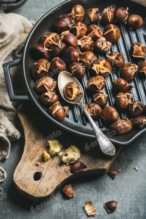 Preview: Roasted chestnuts in cast iron grilling pan over wooden board