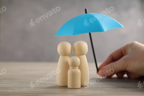 Preview: Woman holding umbrella over human figures at wooden table, closeup. Insurance concept