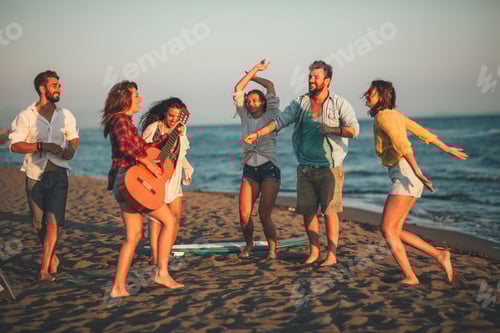 Preview: Happy friends sitting on the beach singing and playing guitar during the sunset