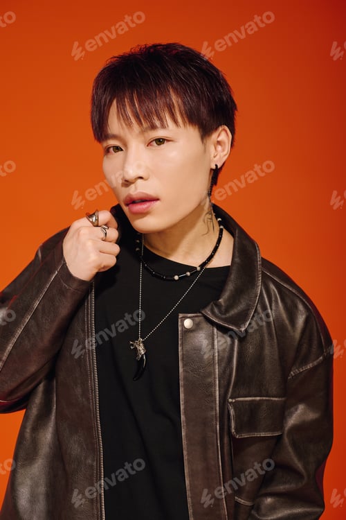 Preview: Stylish young asian man poses confidently against a vibrant orange backdrop showcasing modern flair