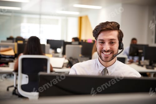 Preview: Young man working at computer with headset in busy office