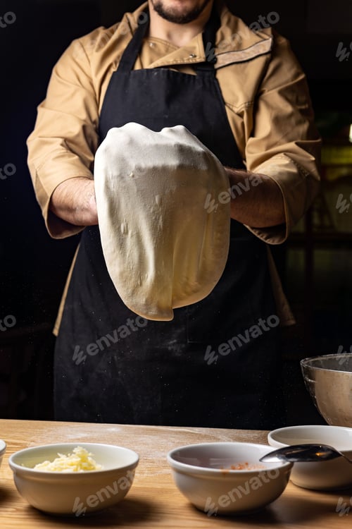 Preview: Young Caucasian male stands in front of a countertop in a kitchen kneading a dough for pizza