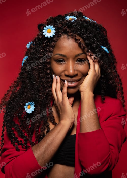 Preview: Smiling Hispanic woman with curly hair and daisies wearing red blazer on red studio background