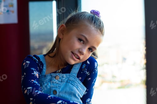 Preview: Portrait of happy caucasian schoolgirl sitting at window in classroom at elementary school