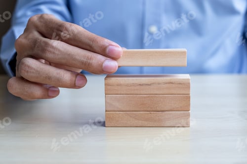 Preview: Businessman hand holding wooden building blocks on table background.