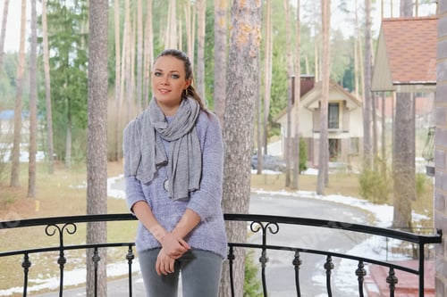 Preview: attractive lady in sweater and scarf standing on balcony