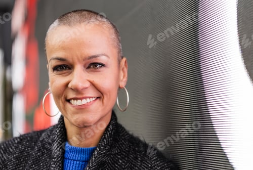 Preview: Smiling businesswoman with shaved head posing in modern office
