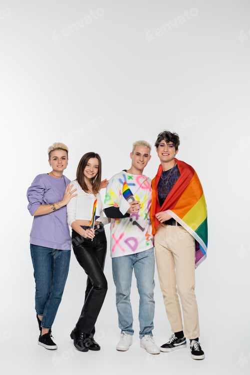 Preview: full length of different identity people with lgbtq flags smiling at camera on grey background