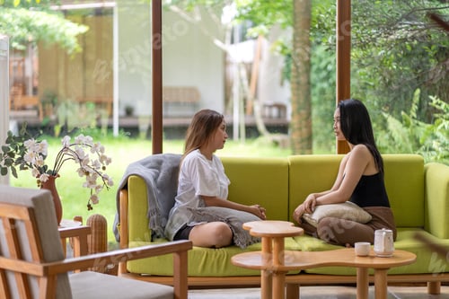 Preview: Two Asian women relaxing and chatting in a bright cozy living room