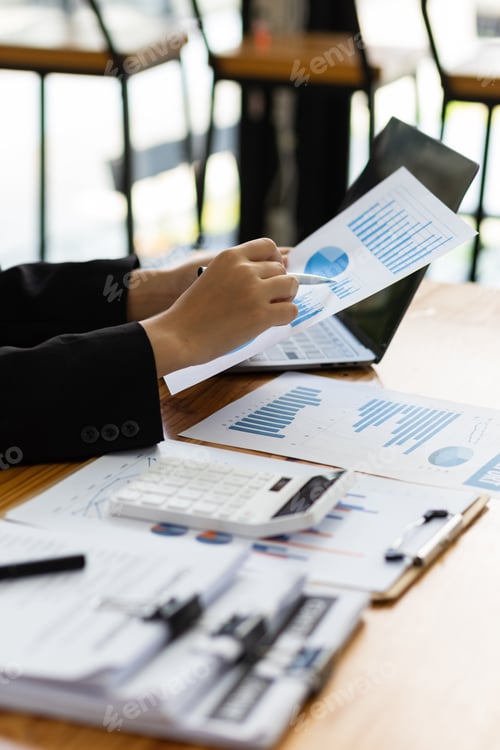Preview: Businesswoman working paperwork, Analysis financial report document and investment chart on laptop.