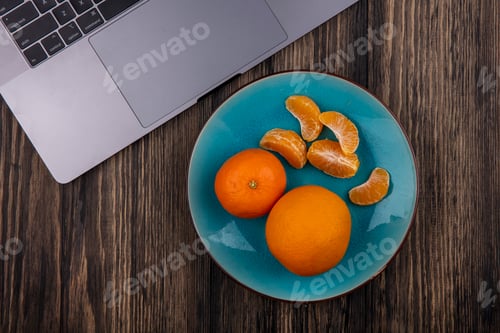 Preview: top view oranges with peeled wedges on a blue plate and a laptop on a wooden background