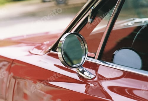 Preview: Closeup shot of a red car side mirror at daytime with a blurry background
