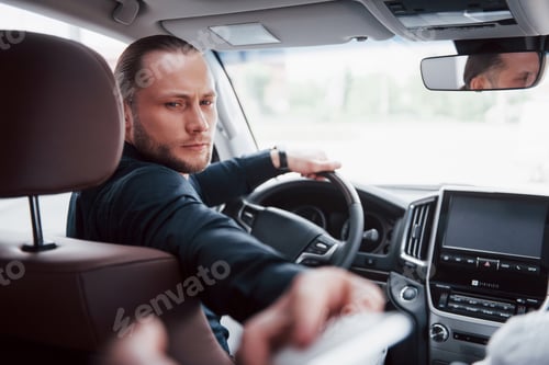 Preview: Confident young businessman sitting at the wheel of his new car