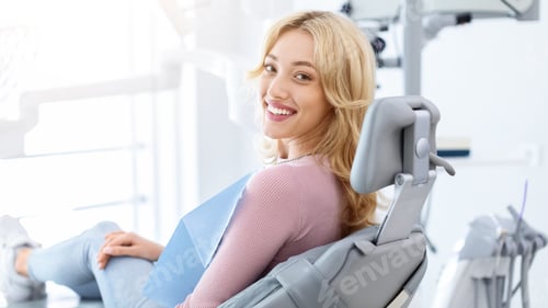 Preview: Smiling and relaxed young woman sitting at dental chair