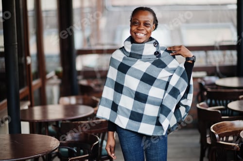 Preview: African woman in checkered cape posed outdoor cafe terrace.