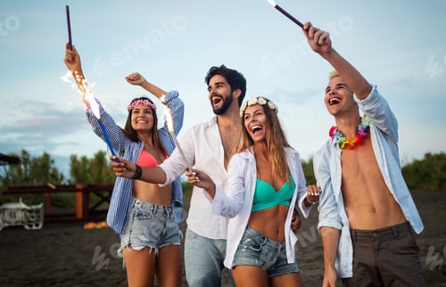Preview: Group of friends having fun running on the beach with sparklers