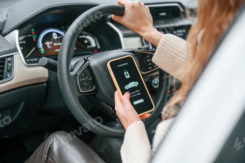 Preview: Sitting by steering wheel and holding smartphone that shows charging process
