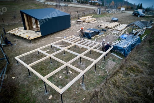 Preview: Man worker building wooden frame house on pile foundation.