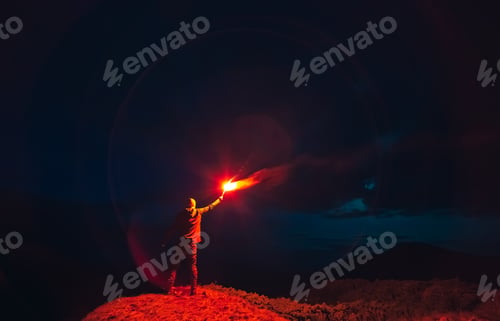 Preview: The man with a red firework stick standing on a night mountain.