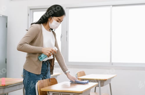 Preview: Young Asian female Teacher in a medical mask cleans up the desk in the classroom