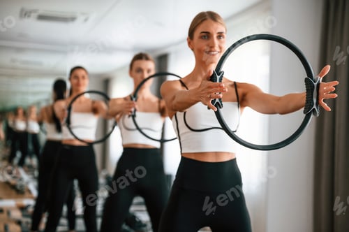 Preview: Standing, smiling, holding circle in hands. Women in fitness center are doing exercises