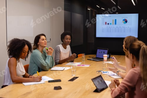 Preview: Diverse casual businesswomen in discussion using tablet and laptop in meeting room
