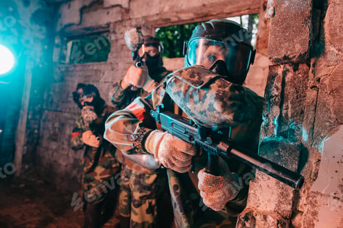 Preview: selective focus of paintball team in uniform and protective masks playing paintball with marker guns
