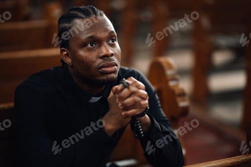Preview: Young priest praying in church holding rosary beads and looking upwards