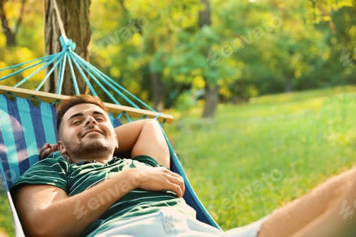 Preview: Young man resting in comfortable hammock at green garden