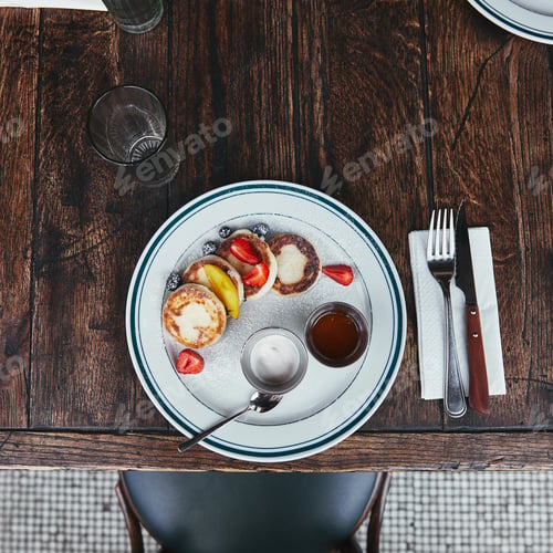 Preview: top view of tasty curd pancakes with bowls of dippings and cutlery on wooden table at restaurant