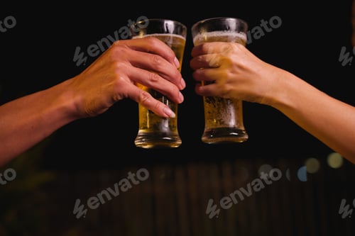Preview: Close-up of friends clinking glasses of beer, celebrating together at a bar.The lively atmosphere