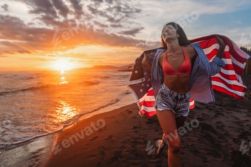 Preview: Happy woman holding american USA flag and running on the beach. Independence Day, travel concept